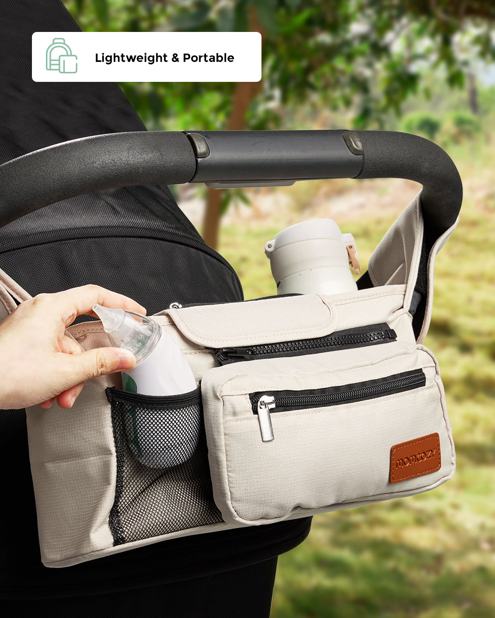 Momcozy stroller organizer bag in beige, with a baby nasal aspirator being placed into a mesh pocket.