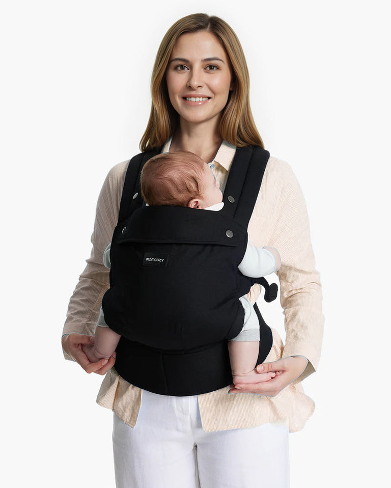 Translation missing: en.Momcozy PureHug Baby Carrier. Black carrier, comfortable design, worn by mother holding baby. Ideal for babywearing